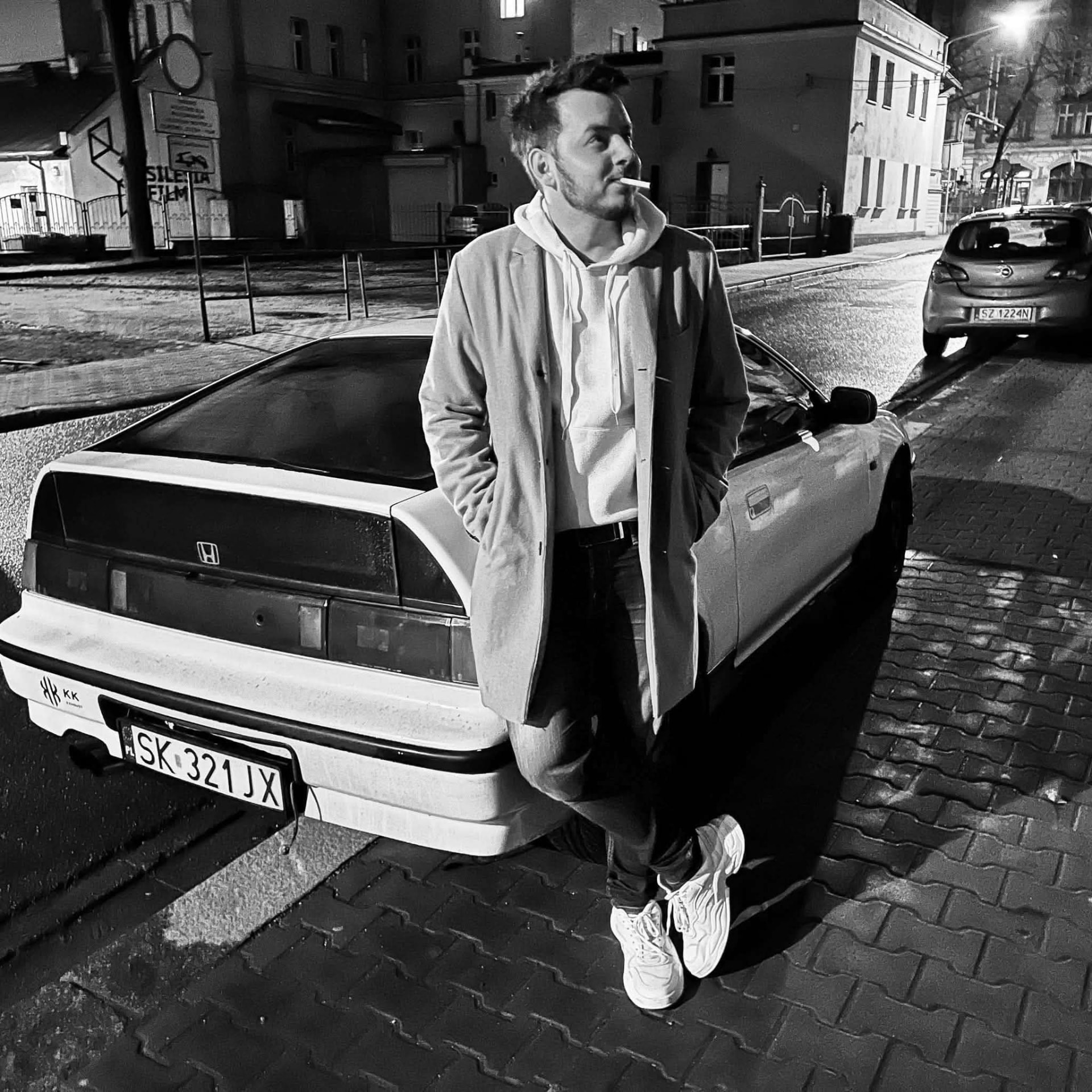 Bartłomiej, założyciel WALLYS, oparty o klasyczny biały samochód na nocnej ulicy